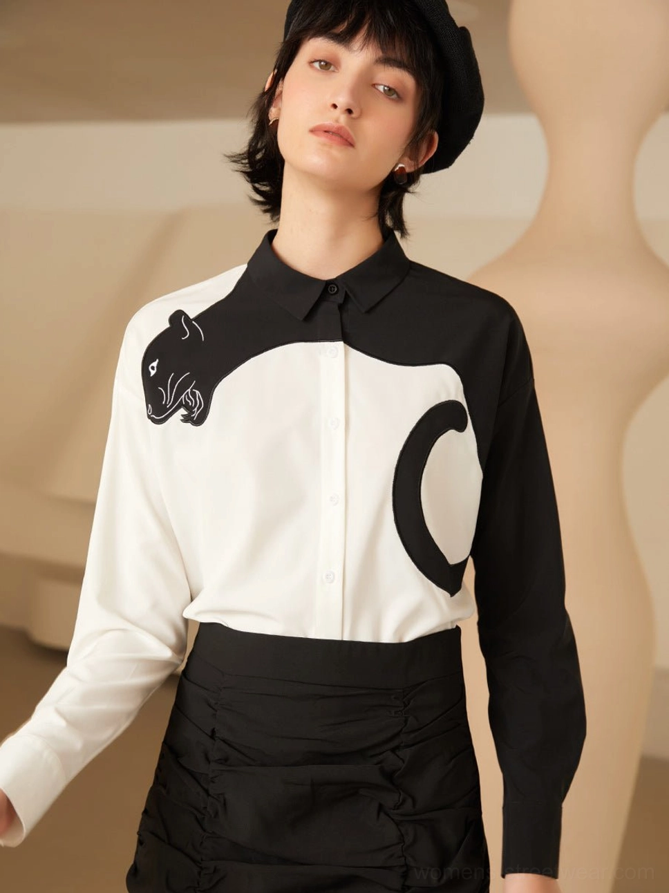 Front view of black and white panther embroidered color block blouse styled with a black beret and ruched midi skirt