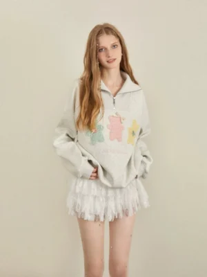 Front full body view of oversized heather grey pastel bear trio quarter zip sweatshirt with three colorful bear appliques styled with a white ruffle mini skirt