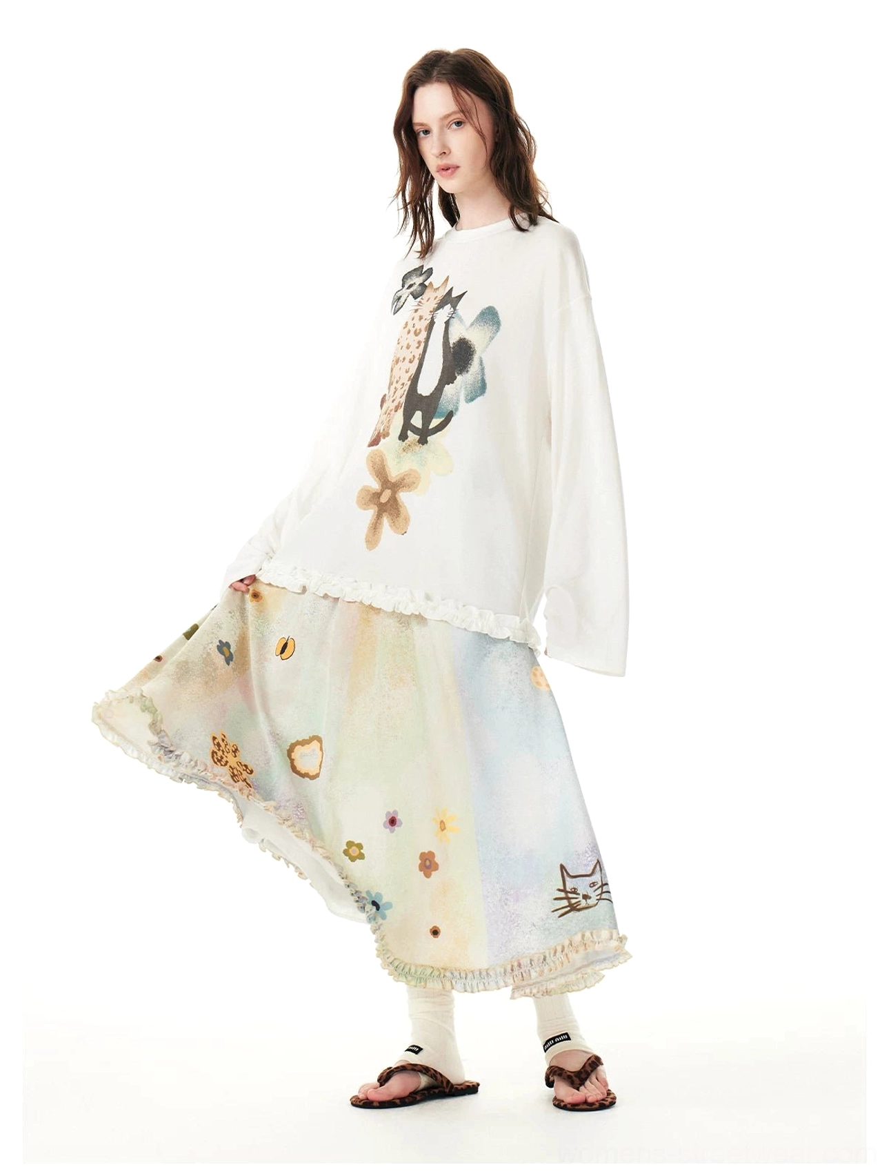 Side view of a Korean streetwear pastel cat print maxi skirt styled with a graphic long sleeve top, leg warmers, and brown sandals