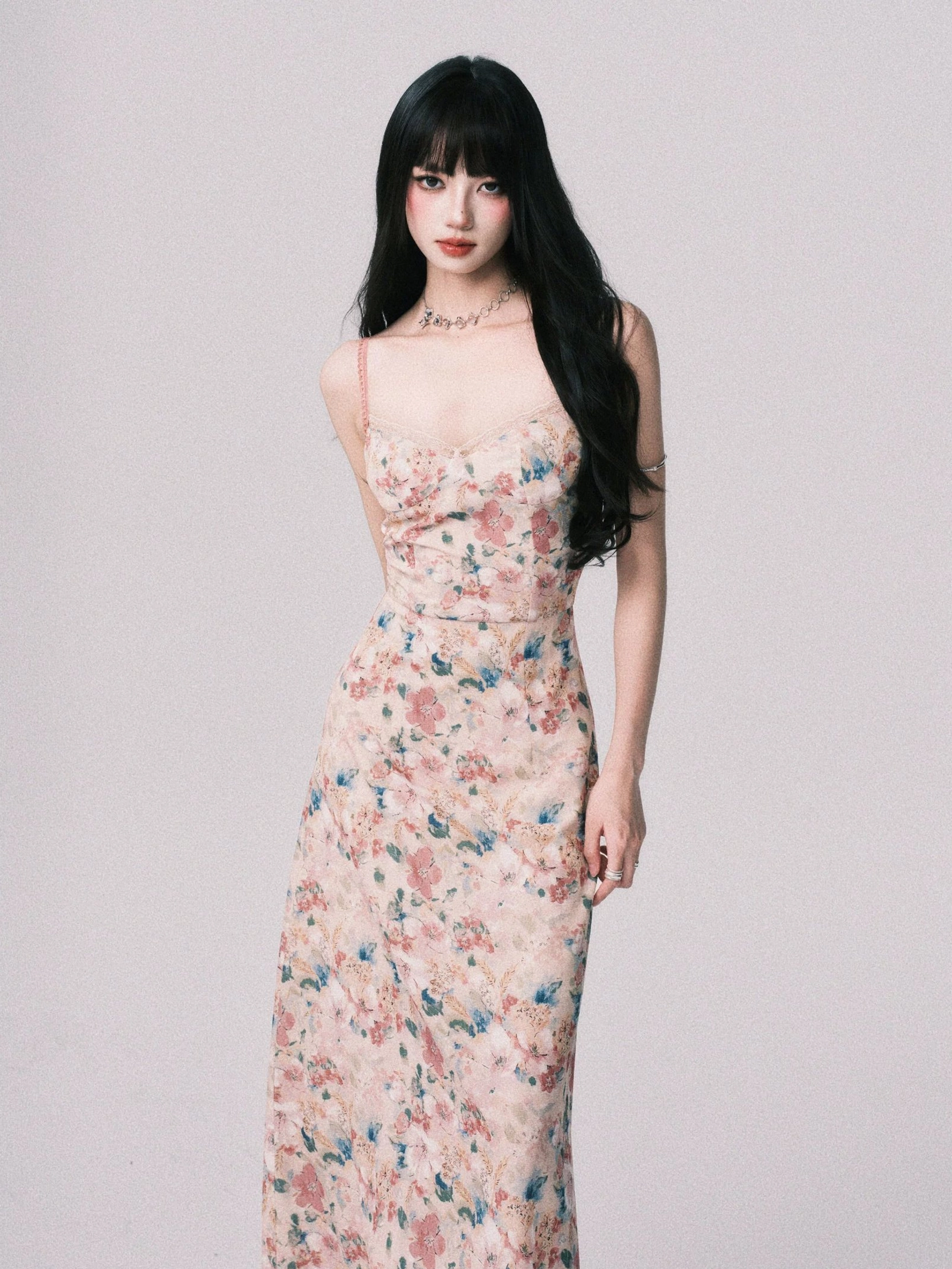 Three quarter view of a romantic blush floral maxi slip dress with ruched bodice, tailored waist, pastel watercolor blooms, and delicate necklace styling