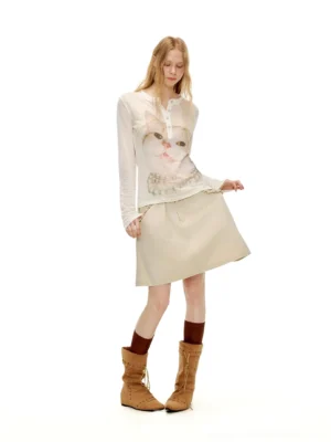 Side view of pearl kitty portrait sheer Henley long sleeve top styled with a beige mini skirt and suede boots