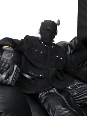 Three-quarter front view of a pearl studded black bouclé streetwear jacket with a relaxed structured fit, padded shoulders, four front pockets, frayed trims, and textured wool-blend fabric styled with tactical accessories