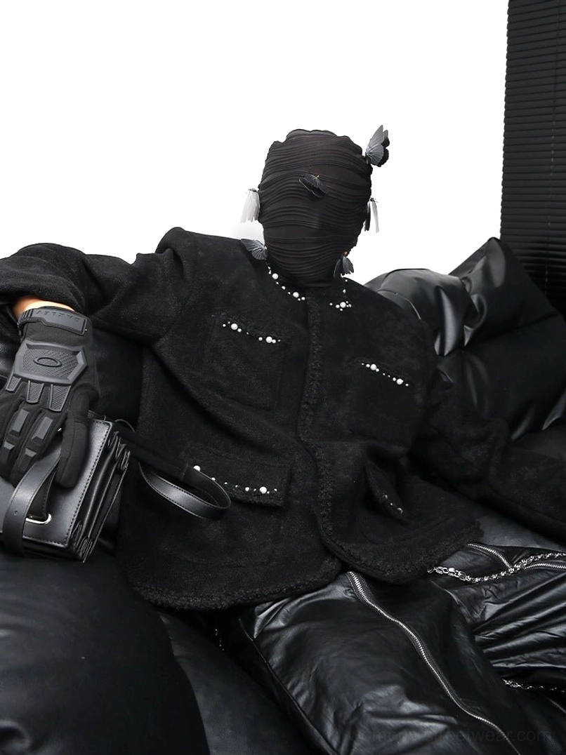 Three-quarter front view of a pearl studded black bouclé streetwear jacket with a relaxed structured fit, padded shoulders, four front pockets, frayed trims, and textured wool-blend fabric styled with tactical accessories