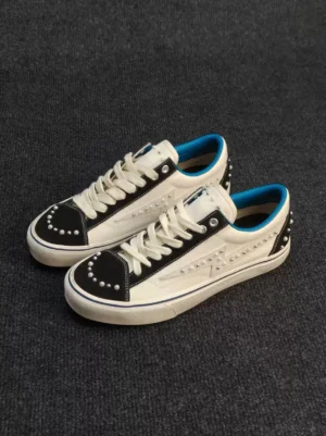 Three-quarter view of white and black pearl-studded low-top skate sneakers with blue trim, embellished toe caps, contrast panels, and rubber soles