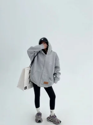 Heather gray oversized pearl trim zip-up hoodie for women styled with black cap leggings and chunky sneakers