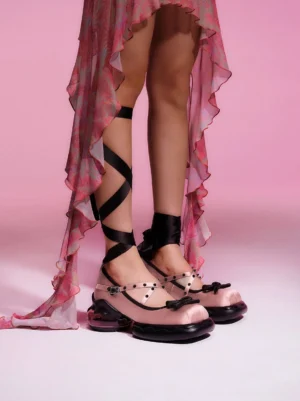 Model wearing pink and black bow platform Mary Jane shoes with cross-wrap straps and a ruffled sheer skirt in romantic Y2K streetwear style