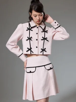 Front view of pink cropped jacket and pleated mini skirt with black bow details and contrast trim