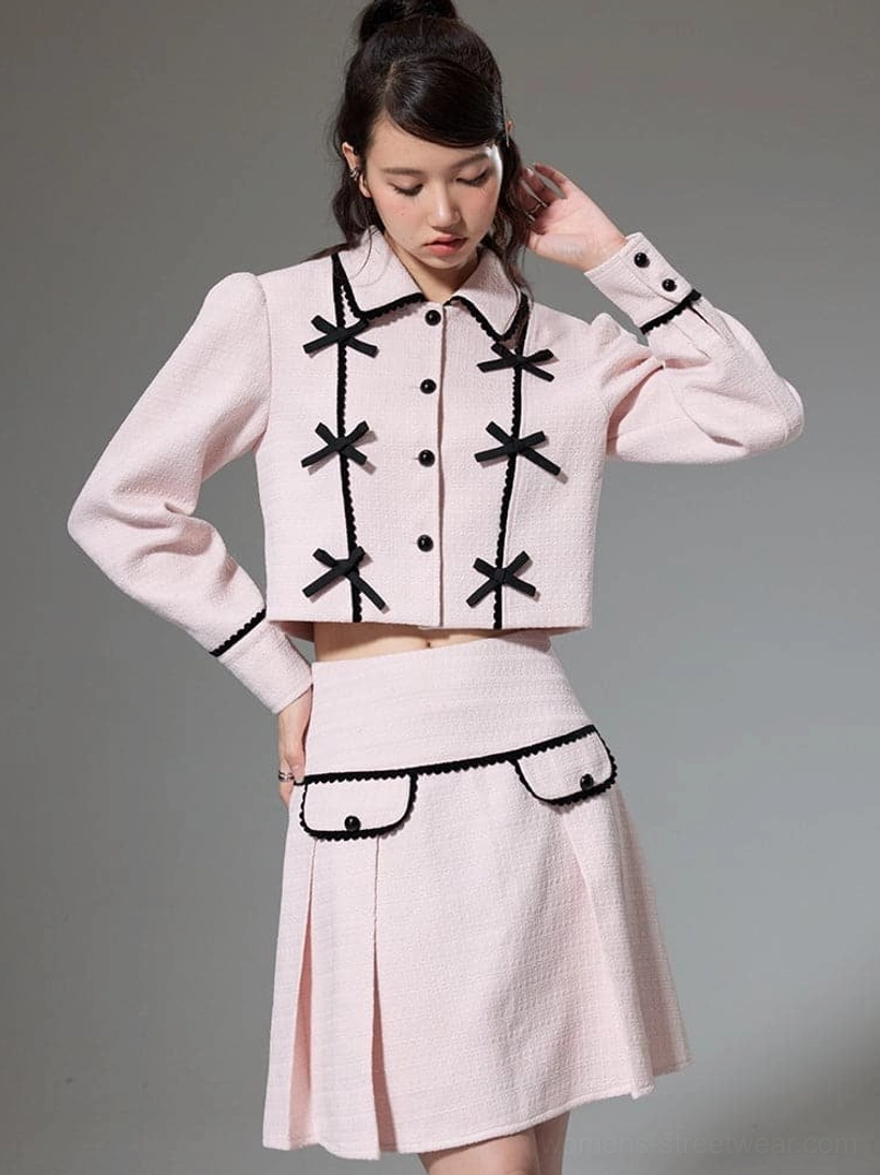 Front view of pink cropped jacket and pleated mini skirt with black bow details and contrast trim