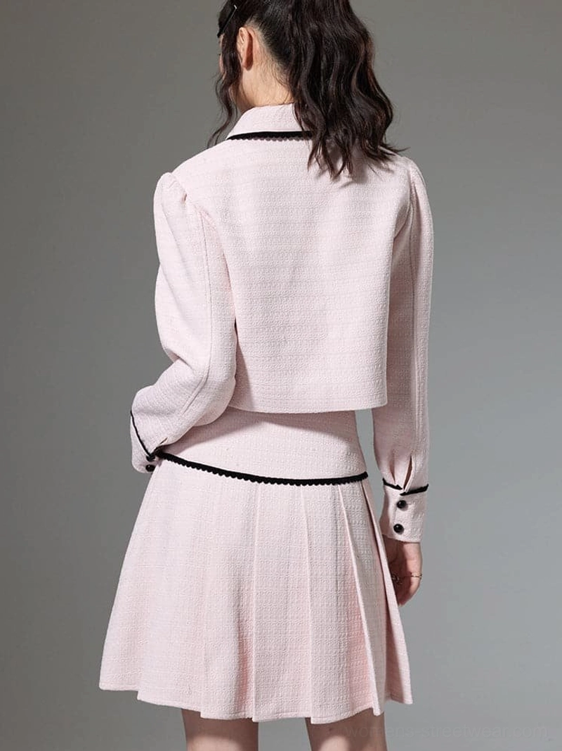 Back three quarter view of pink bow trim cropped jacket and pleated mini skirt with black edging