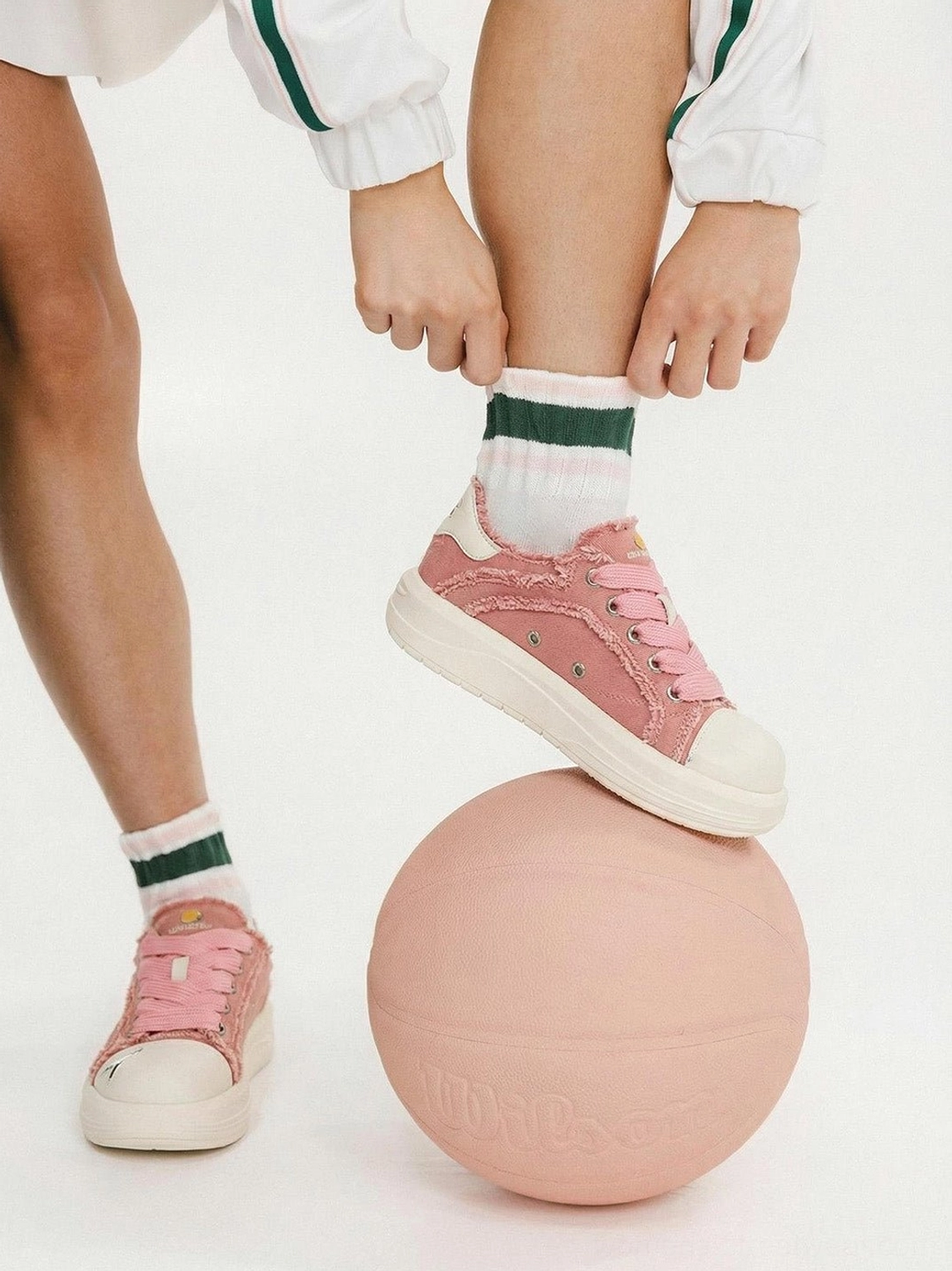 Pink canvas platform skate sneaker worn with striped cuff socks while resting on a pink basketball in a playful Y2K streetwear scene