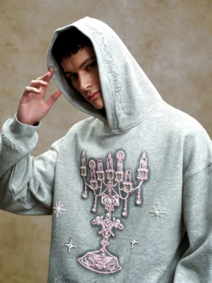 Close-up portrait showing the pink 3D chandelier embroidery, gem-style embellishments, structured hood, and decorative script details on an oversized streetwear hoodie