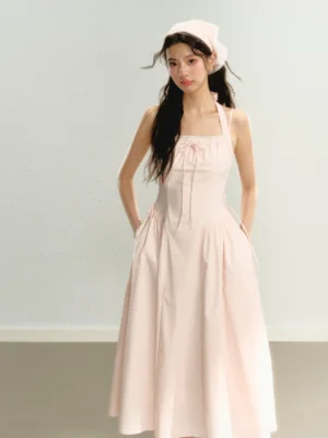 Rear three-quarter view of a pink halter midi sundress showing the gathered waist, flowing skirt, hidden side pockets, matching headscarf, and feminine Korean streetwear styling