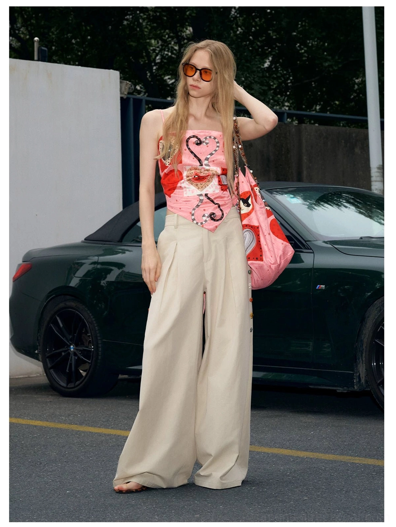 Pink kitty patchwork tote styled with a heart print camisole, wide leg beige trousers, orange sunglasses, and a playful Korean streetwear outfit