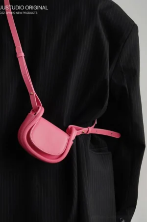 Pink mini saddle crossbody shoulder bag styled at the waist with a black striped suit