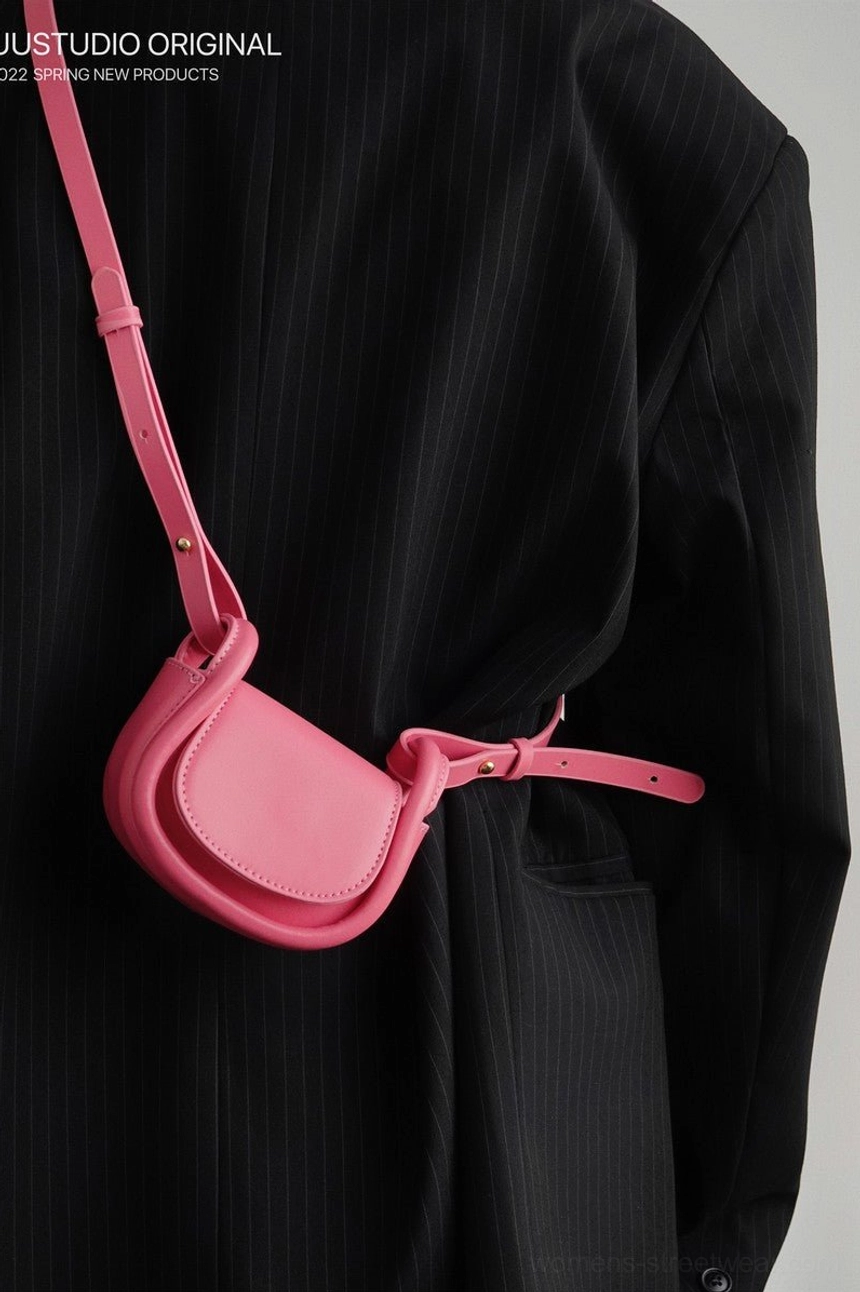 Pink mini saddle crossbody shoulder bag styled at the waist with a black striped suit