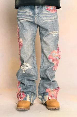 Full-body male model wearing faded blue pink-patch distressed wide-leg streetwear jeans with ripped panels and tan work boots