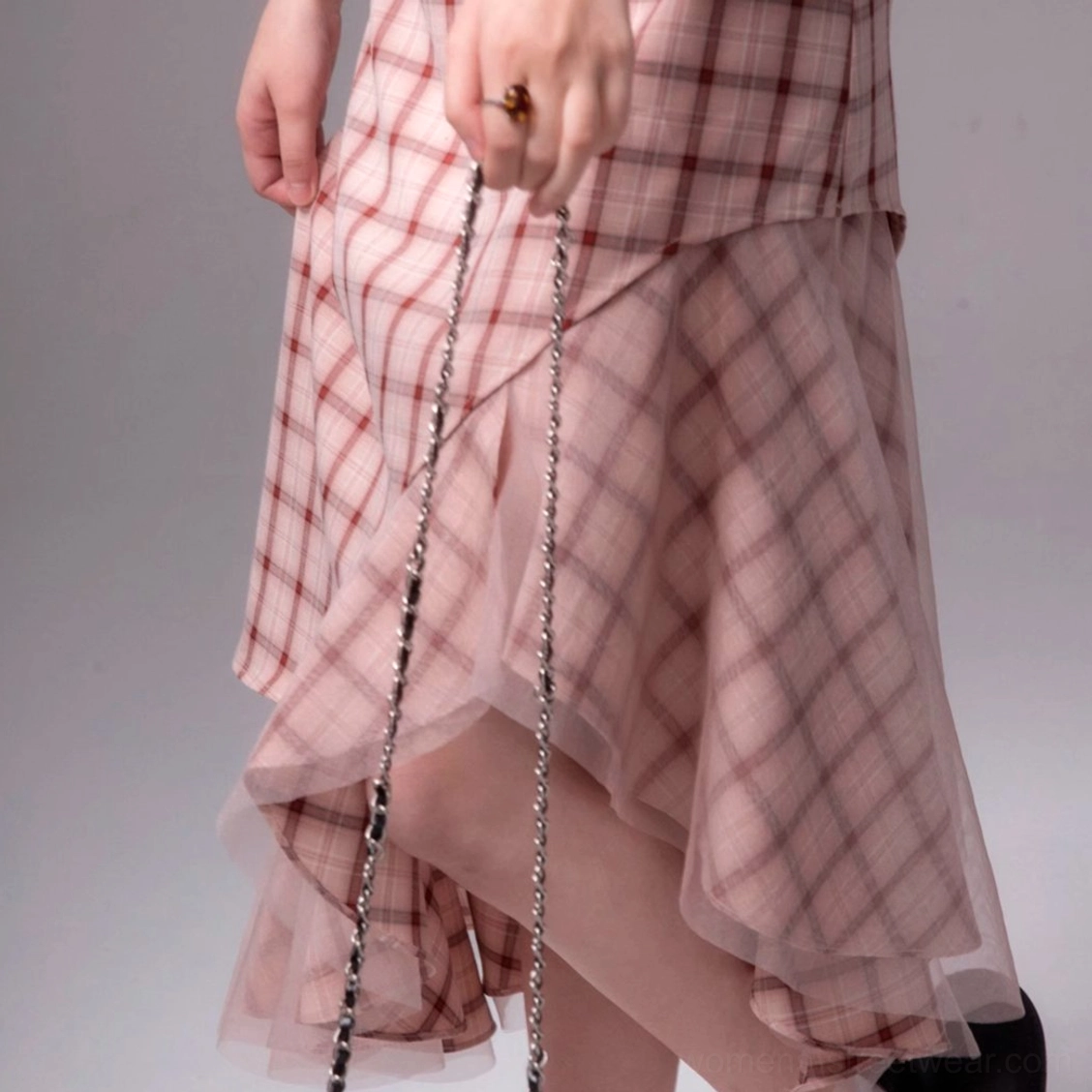 Close-up view of the asymmetric ruffled hem on a pink plaid fitted midi dress with layered overlay