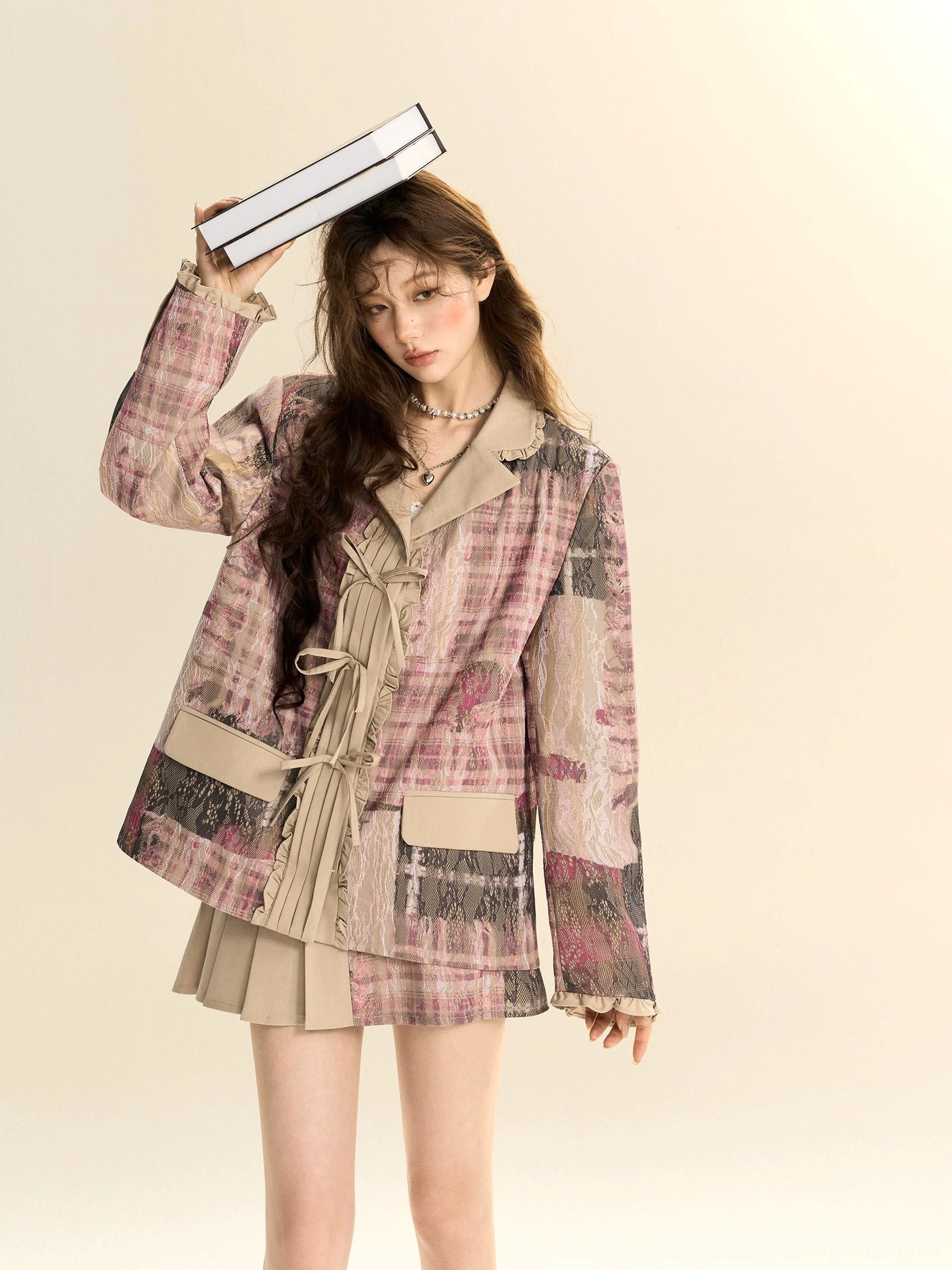 Half-body view of a pink plaid oversized blazer with notched lapels and front pleated tie details styled with a khaki pleated mini skirt
