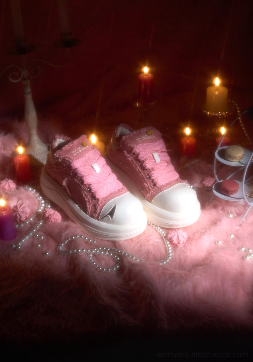 Pair of pink platform skate sneakers displayed on pink fur with candles, pearl chains, macarons, white toe caps, and chunky platform soles