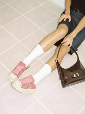 Woman wearing pink platform skate sneakers with white crew socks beside a brown leather handbag in a casual streetwear outfit