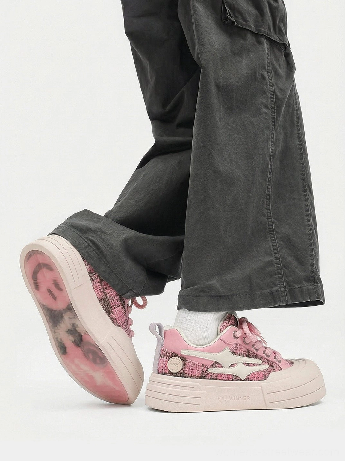 Rear side view of pink platform sneakers with dark gray cargo pants white ankle sock and printed translucent pink outsole