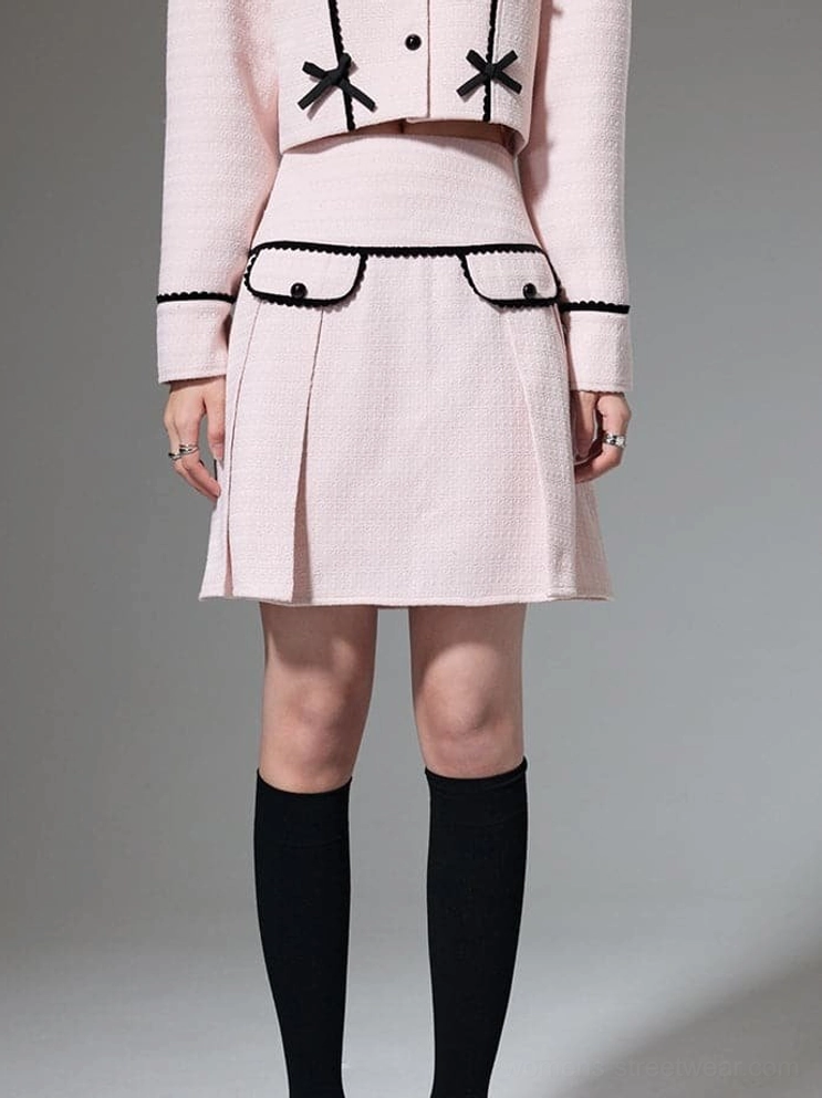 Close up of pink pleated mini skirt and cropped jacket showing black bows and braided pocket trim
