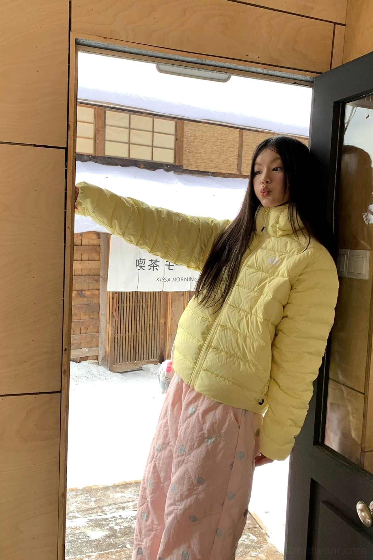 Side silhouette of pink polka dot fleece cuff streetwear pants styled with a yellow winter jacket indoors