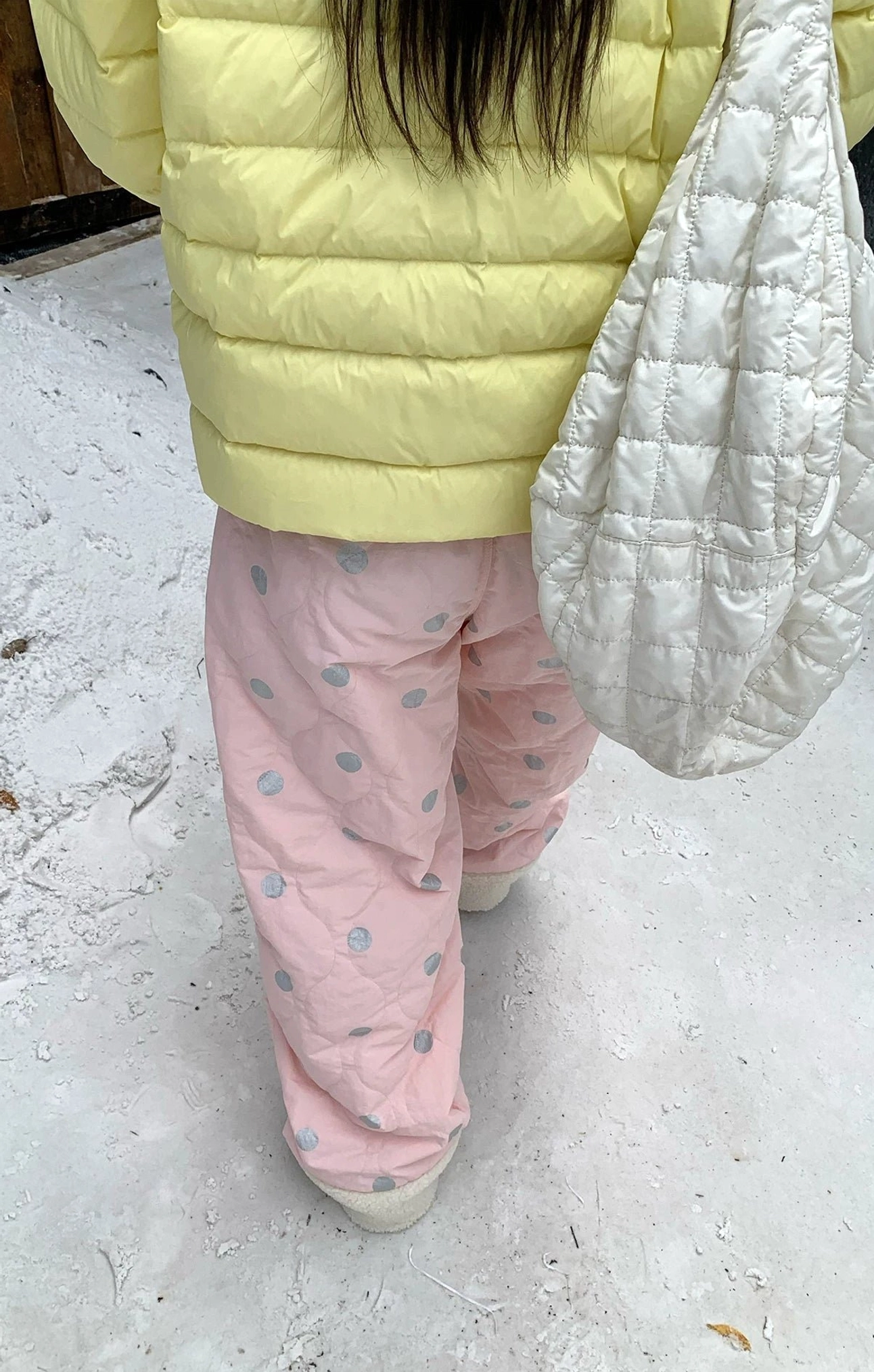 Back view of pink polka dot quilted fleece cuff streetwear pants paired with a yellow puffer jacket in the snow