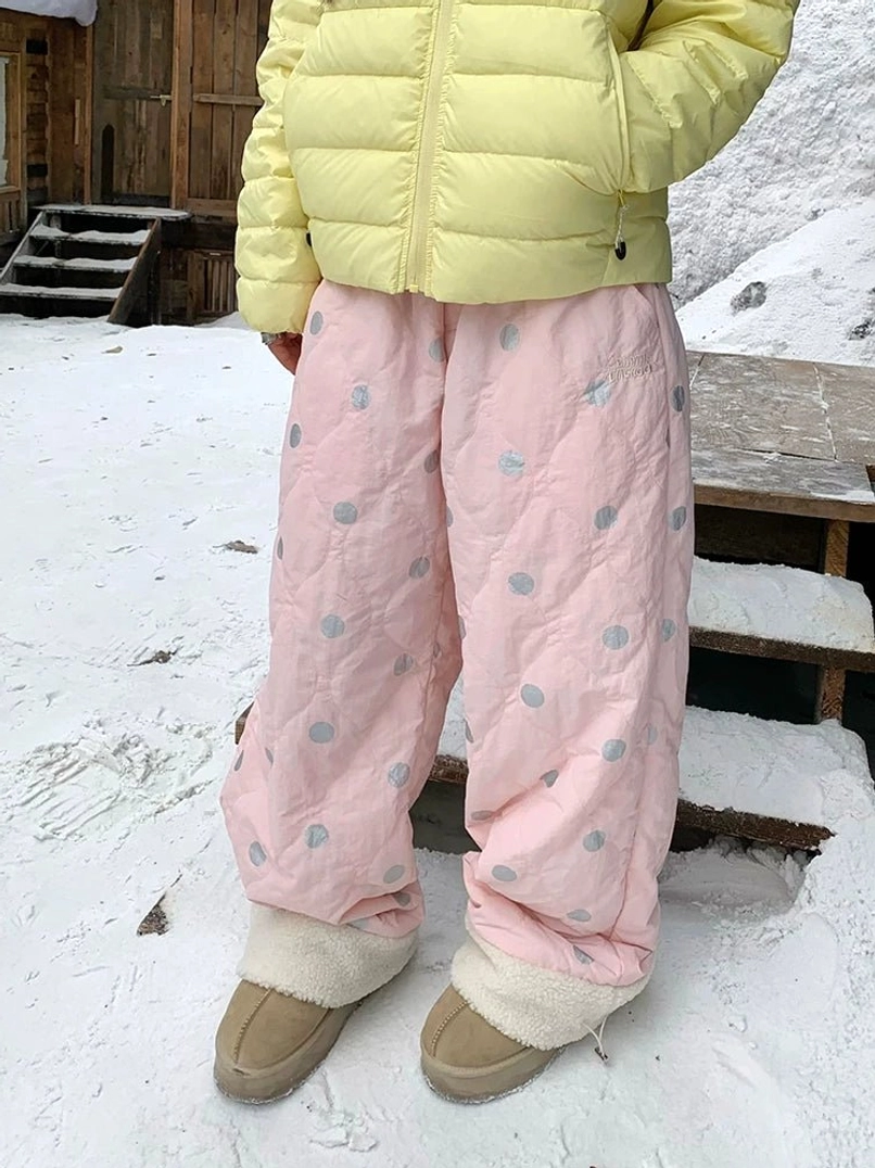 Pink polka dot quilted wide leg streetwear pants with soft sherpa fleece ankle cuffs shown on a snowy wooden platform