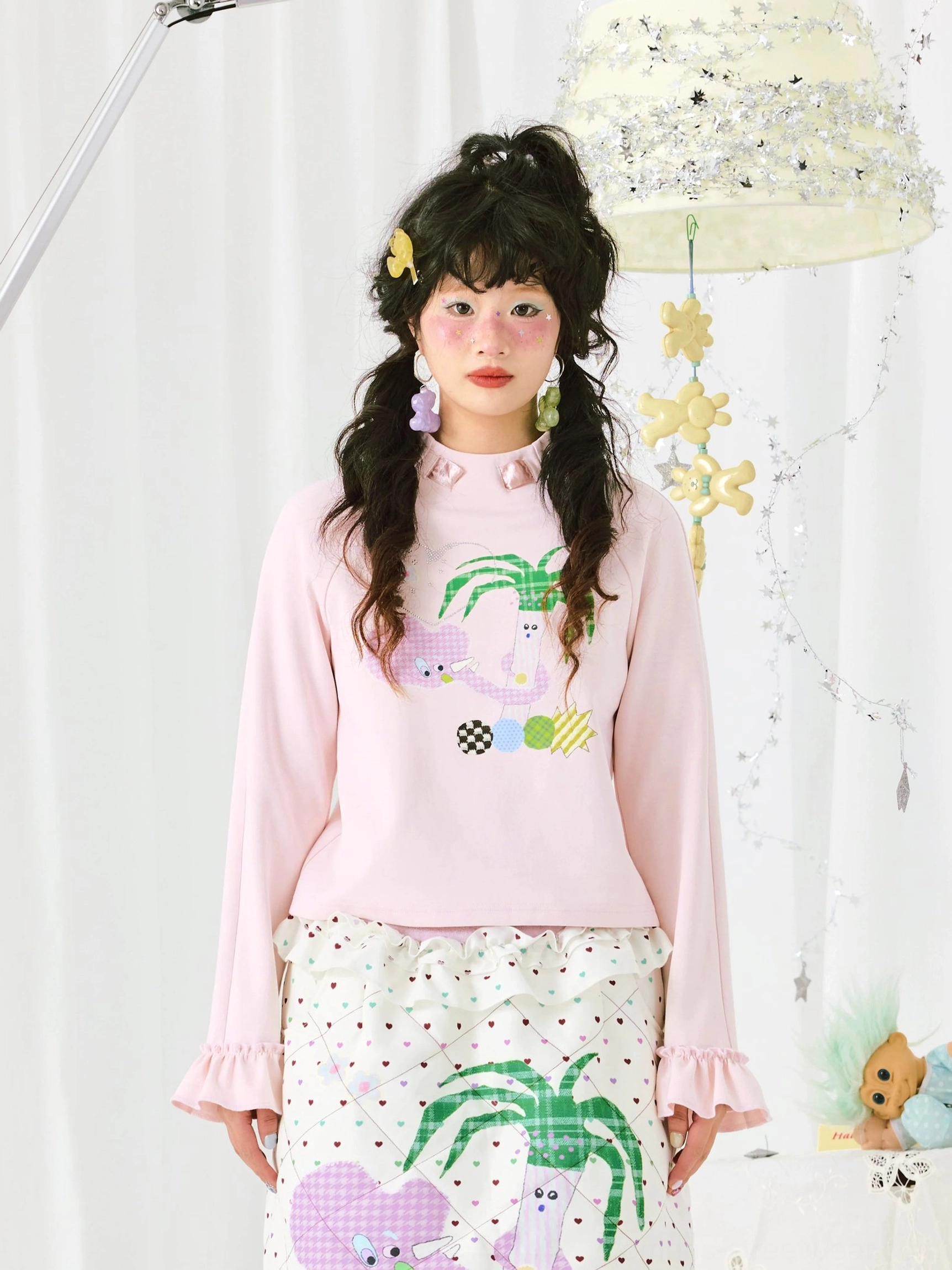 Front view of a pastel pink ruffle sleeve top with bow collar details and cute palm tree print styled with a polka dot midi skirt