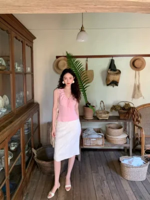 Pink ruffled V-neck tie-front sleeveless blouse paired with a white high-waisted midi skirt in a vintage studio
