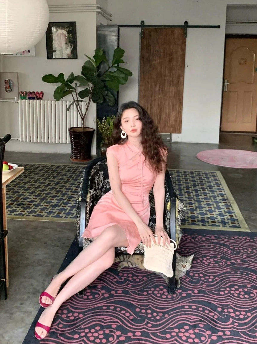 Pink satin cheongsam mini dress shown in a seated full-body view, sleeveless fitted silhouette with glossy finish and romantic Y2K styling