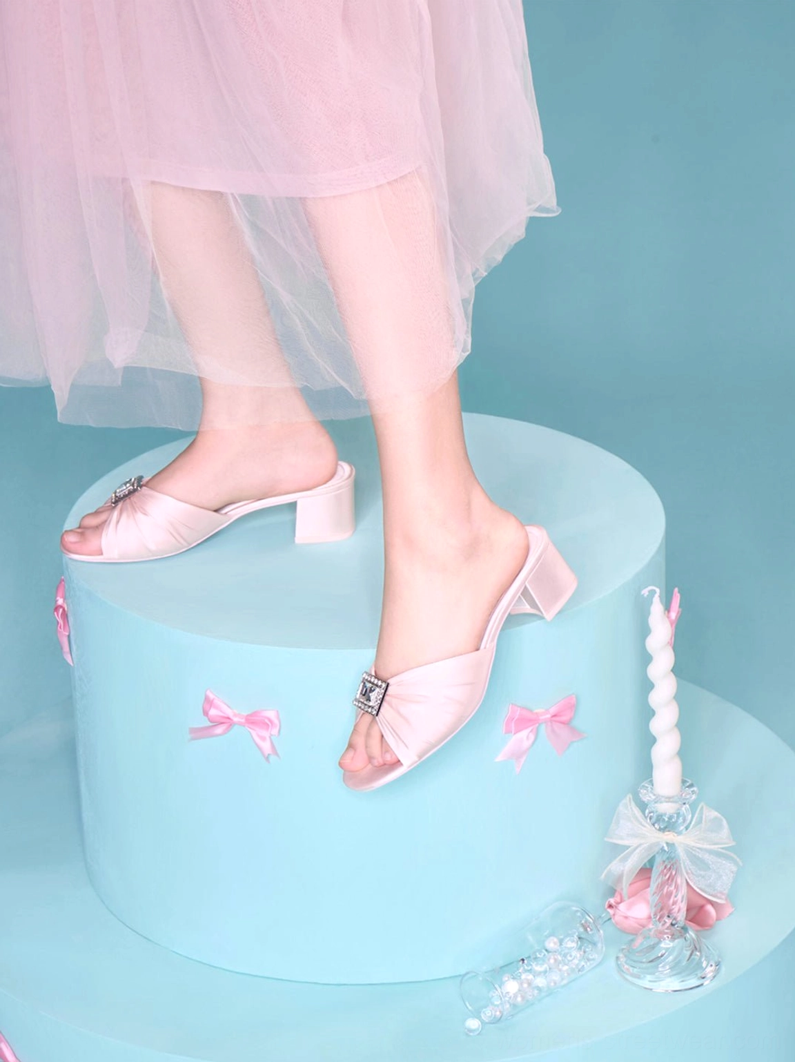 Pink satin crystal-buckle block heel slides displayed with decorative pink bow accents and tulle styling