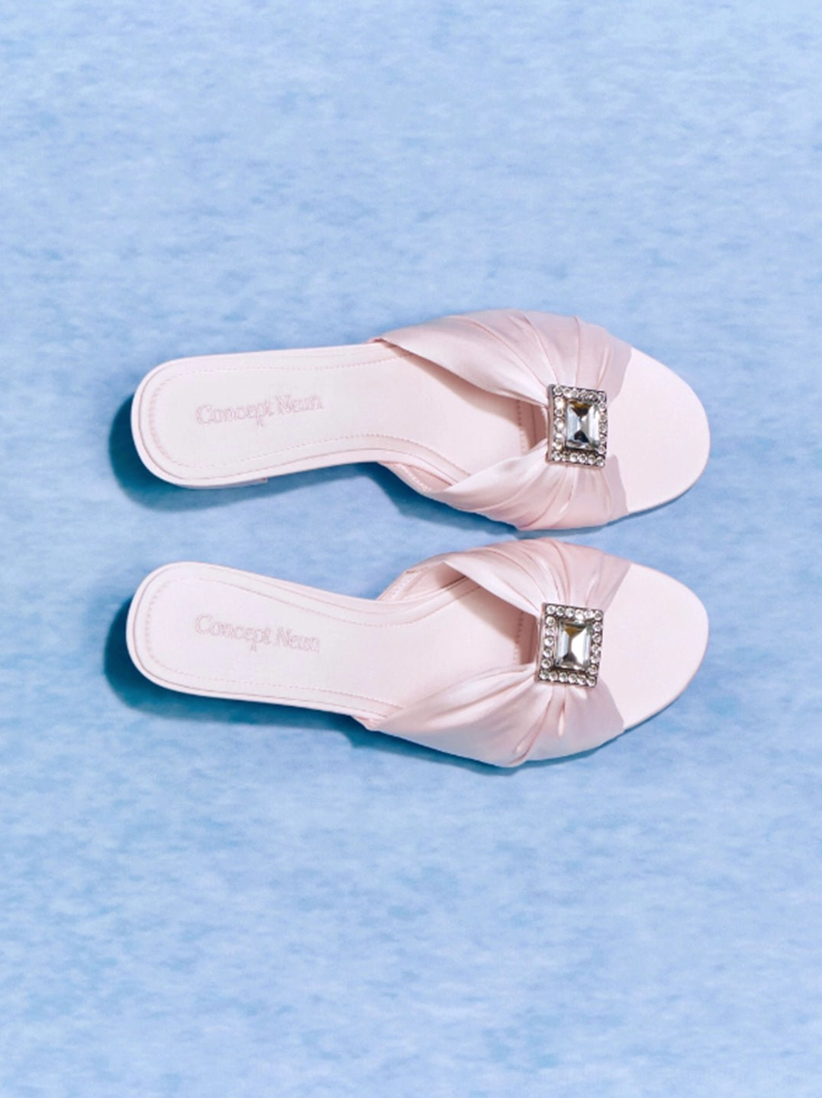 Pair of pink satin crystal-buckle mule slides shown from above with ruched straps and open toes