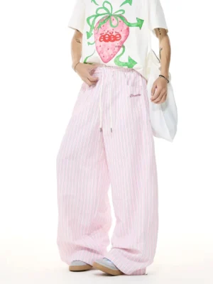 Three-quarter view of relaxed pink stripe wide-leg streetwear pants with drawstring waistband and side pockets styled with a cropped tee and white canvas bag