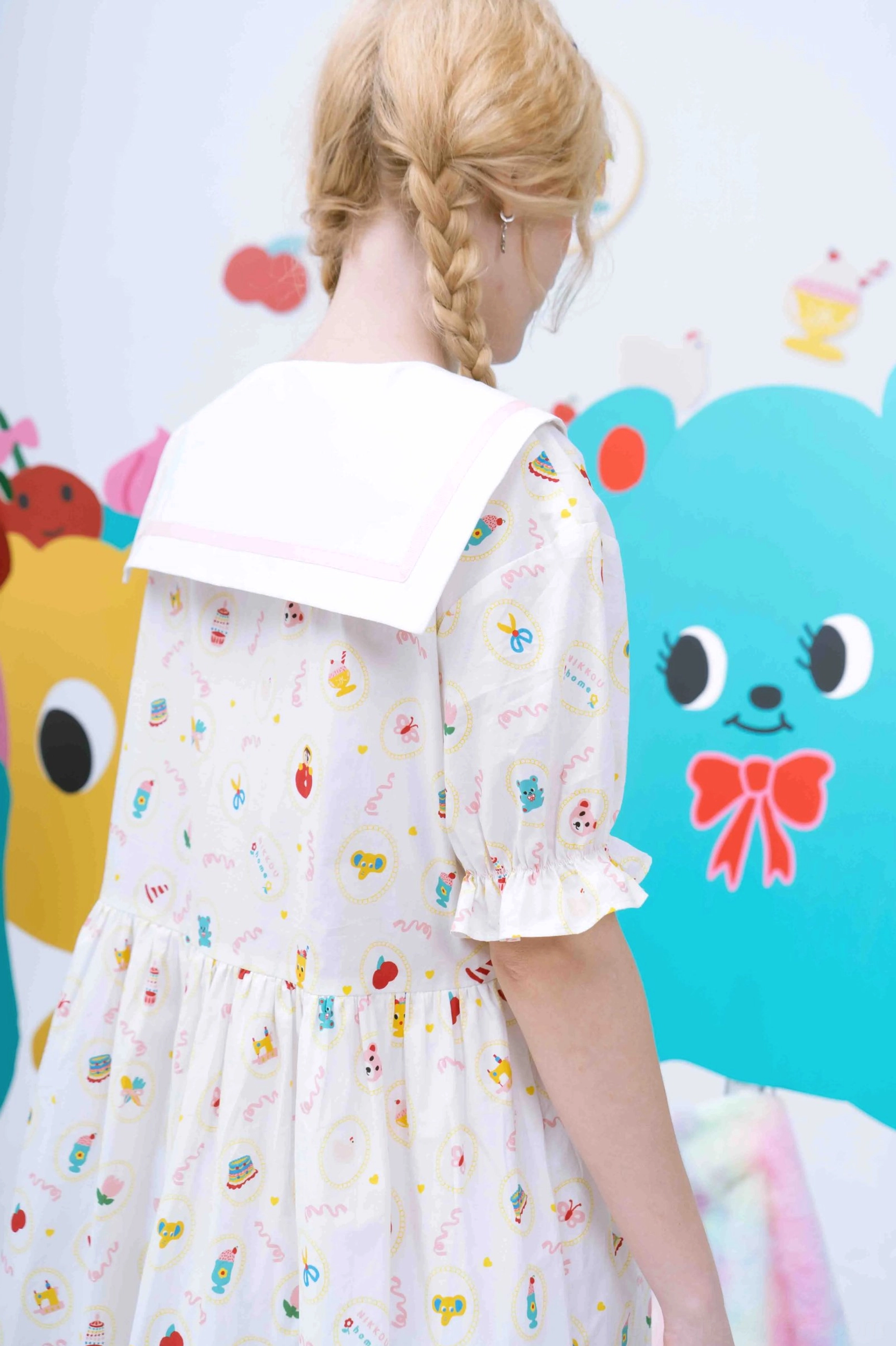 Back view showing the pink trimmed sailor collar ruffled puff sleeves and colorful cartoon motifs on the babydoll dress
