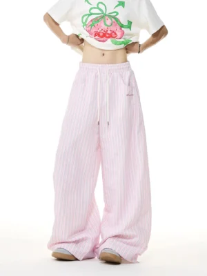 Front view of women's pink and white striped wide-leg streetwear lounge pants with elastic drawstring waist and embroidered waist label styled with a cropped white graphic T-shirt