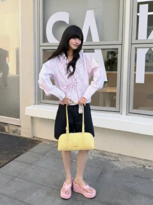 Model styling pink Y2K logo print platform wedge flip-flops with ruffle blouse and black shorts at an outdoor cafe