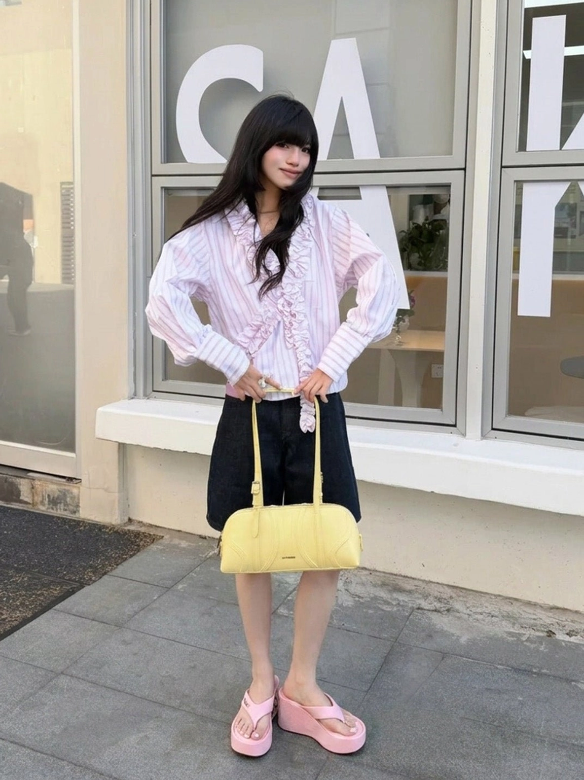 Model styling pink Y2K logo print platform wedge flip-flops with ruffle blouse and black shorts at an outdoor cafe
