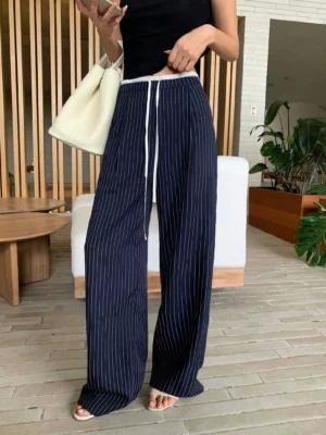 Model wearing navy blue pinstripe wide leg streetwear pants with drawstring waist and black cropped camisole in a modern indoor setting