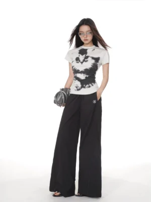 Heather grey pixel cat graphic T-shirt styled with black wide-leg trousers, sandals, sunglasses, and a grey shoulder bag in a modern streetwear outfit