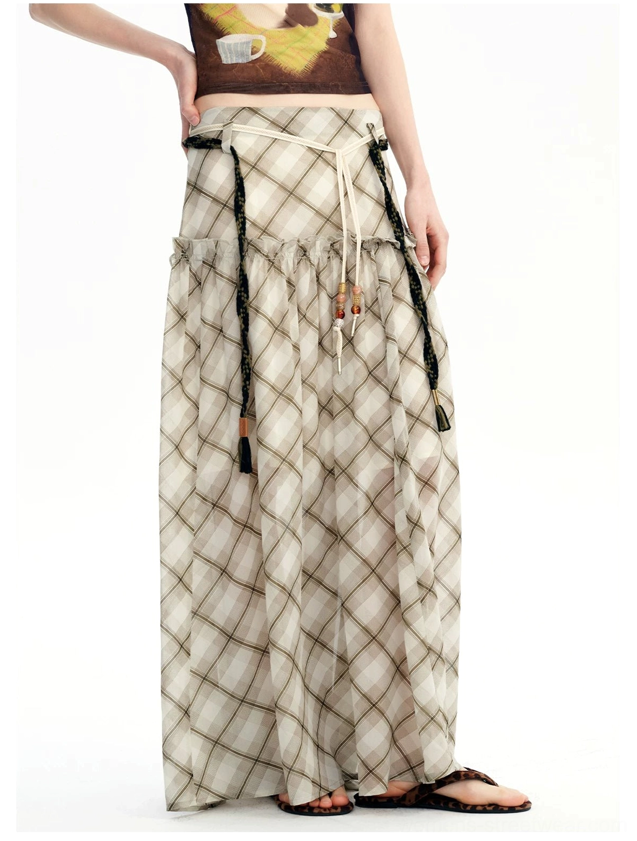 Front three-quarter view of a tiered plaid chiffon maxi skirt with decorative waist straps and soft flowing movement