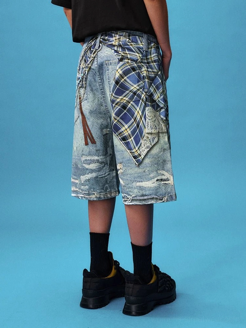 Back view of a model wearing acid washed blue distressed denim jorts with plaid pocket detail, leather tassel accent, black top, socks, and chunky sneakers