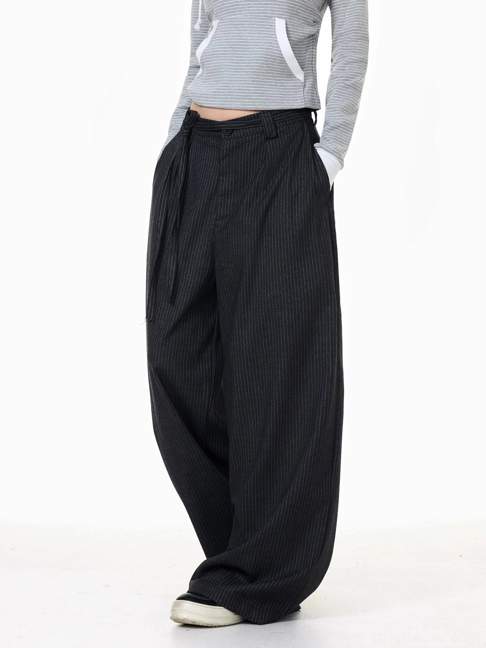 Three-quarter side view of pleated dark gray pinstripe wide-leg trousers with tailored seams and relaxed streetwear volume