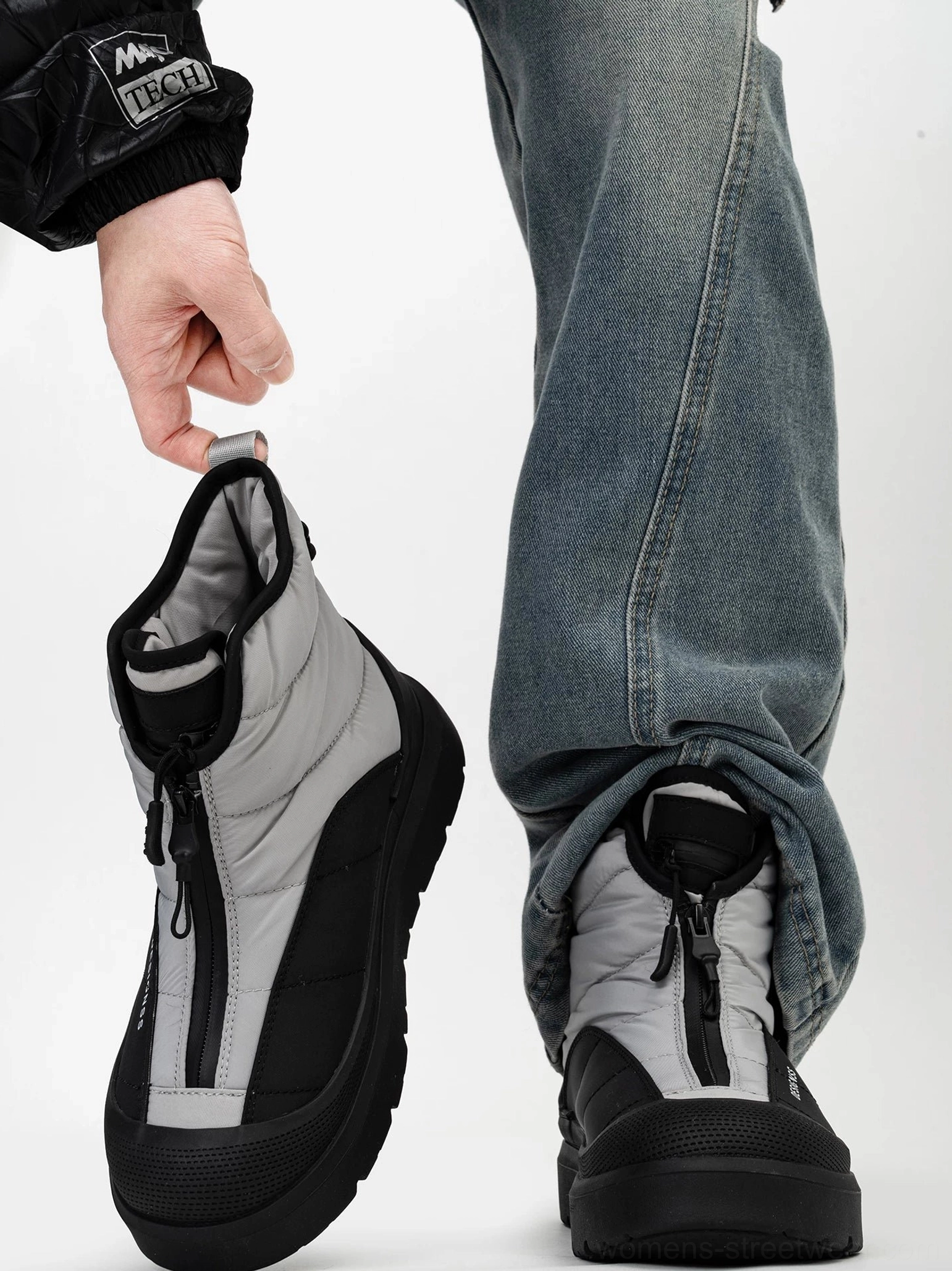 Black and gray Polar Flux zip-up snow boots worn with blue jeans and a black tech jacket, showing the padded quilted upper and chunky platform sole