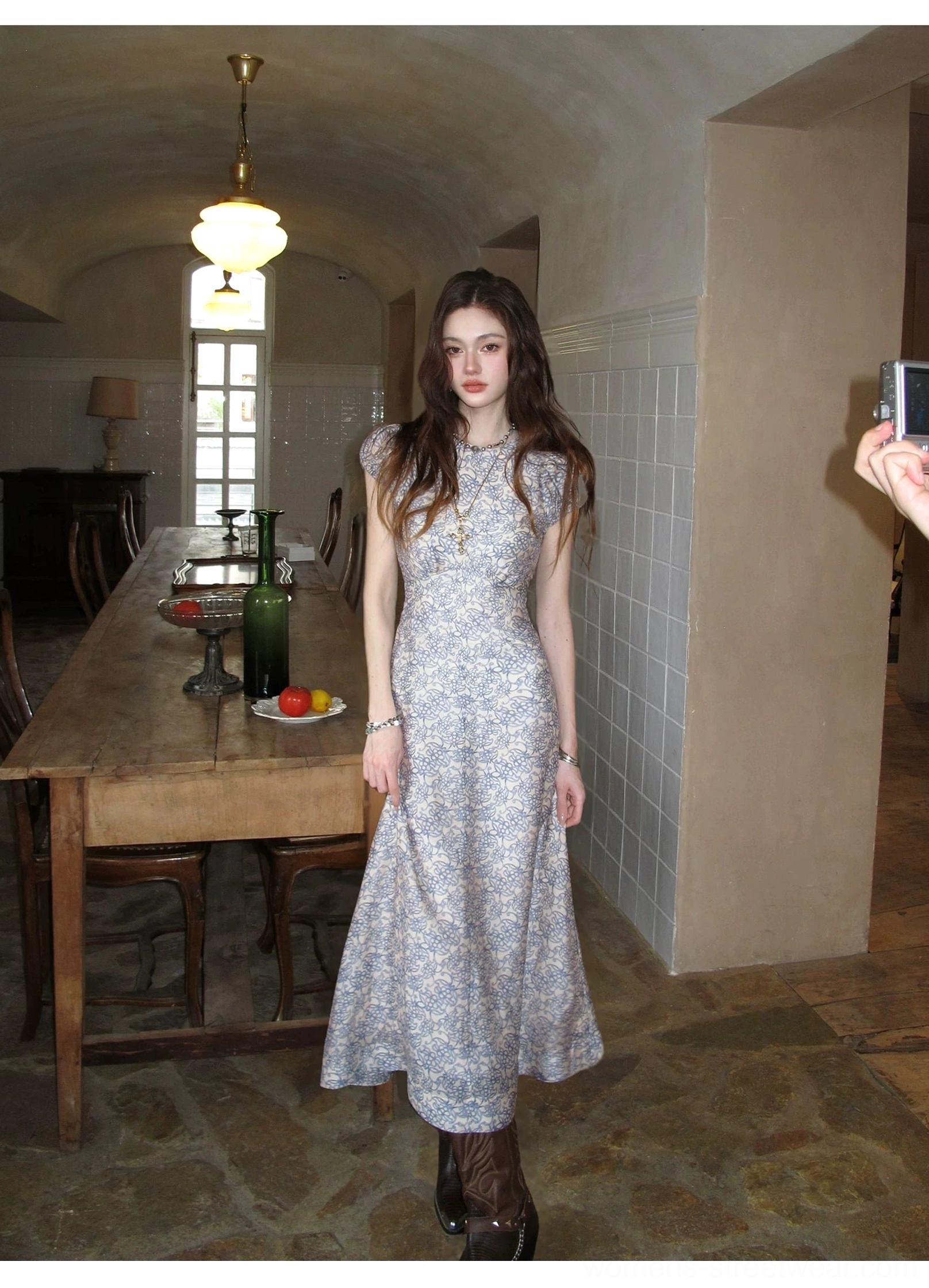 Full front view of a slim porcelain blue floral column maxi dress styled with brown leather mid-calf boots in an elegant vintage dining hall