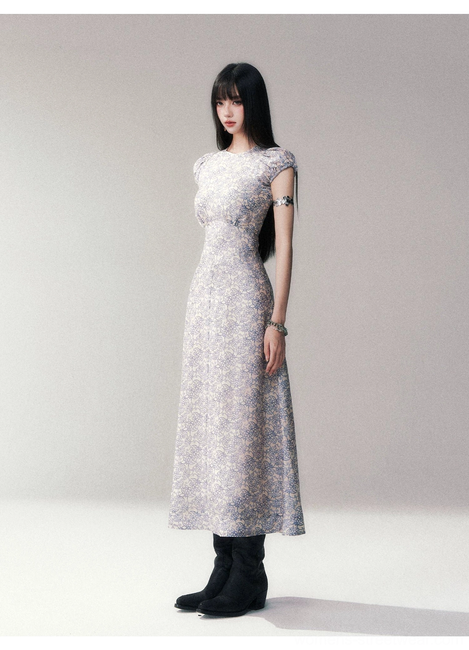 Right three-quarter view of a fitted porcelain blue floral column maxi dress with a sculpted bodice, long skirt, and coordinated silver wrist jewelry