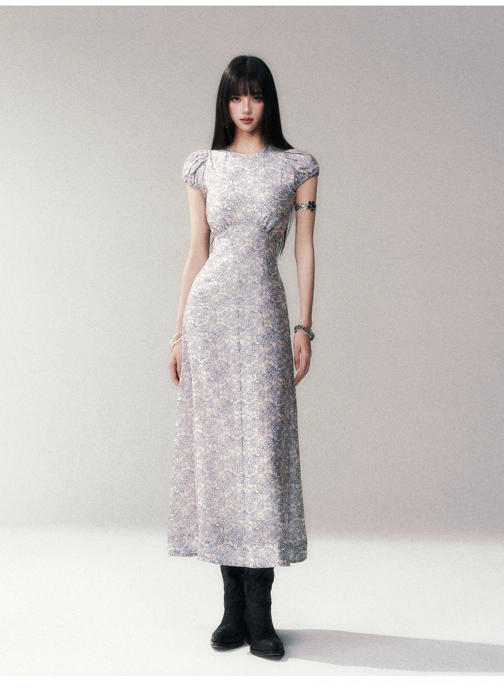 Full front view of a porcelain blue floral maxi dress with ruched shoulder cap sleeves styled with black ankle boots in a minimalist studio