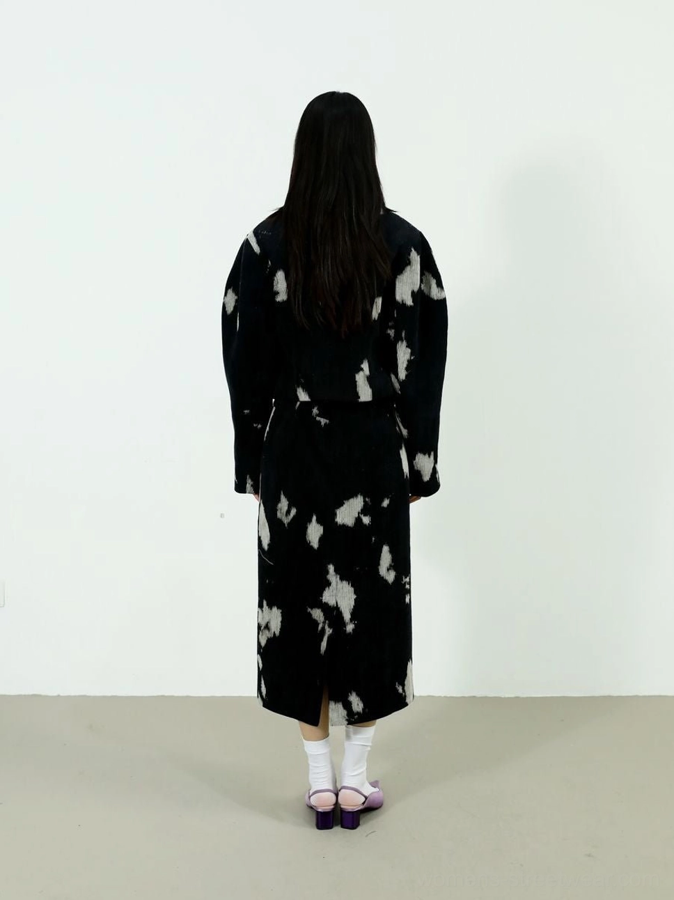 Back view of coordinated black and off-white printed coat and midi skirt outfit with white socks and pointed heels