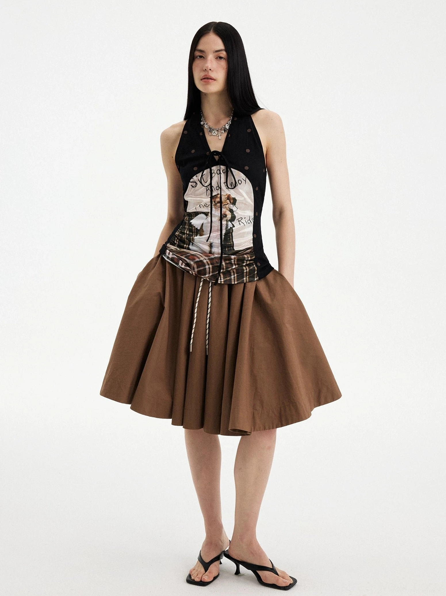 Full body front view of a brown multi puppy print plaid halter top with black polka dots, tie-up neckline, and matching brown skirt